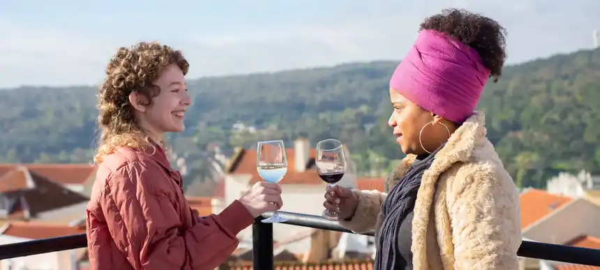 Two friends raising glasses on a rooftop terrace above Lisbon