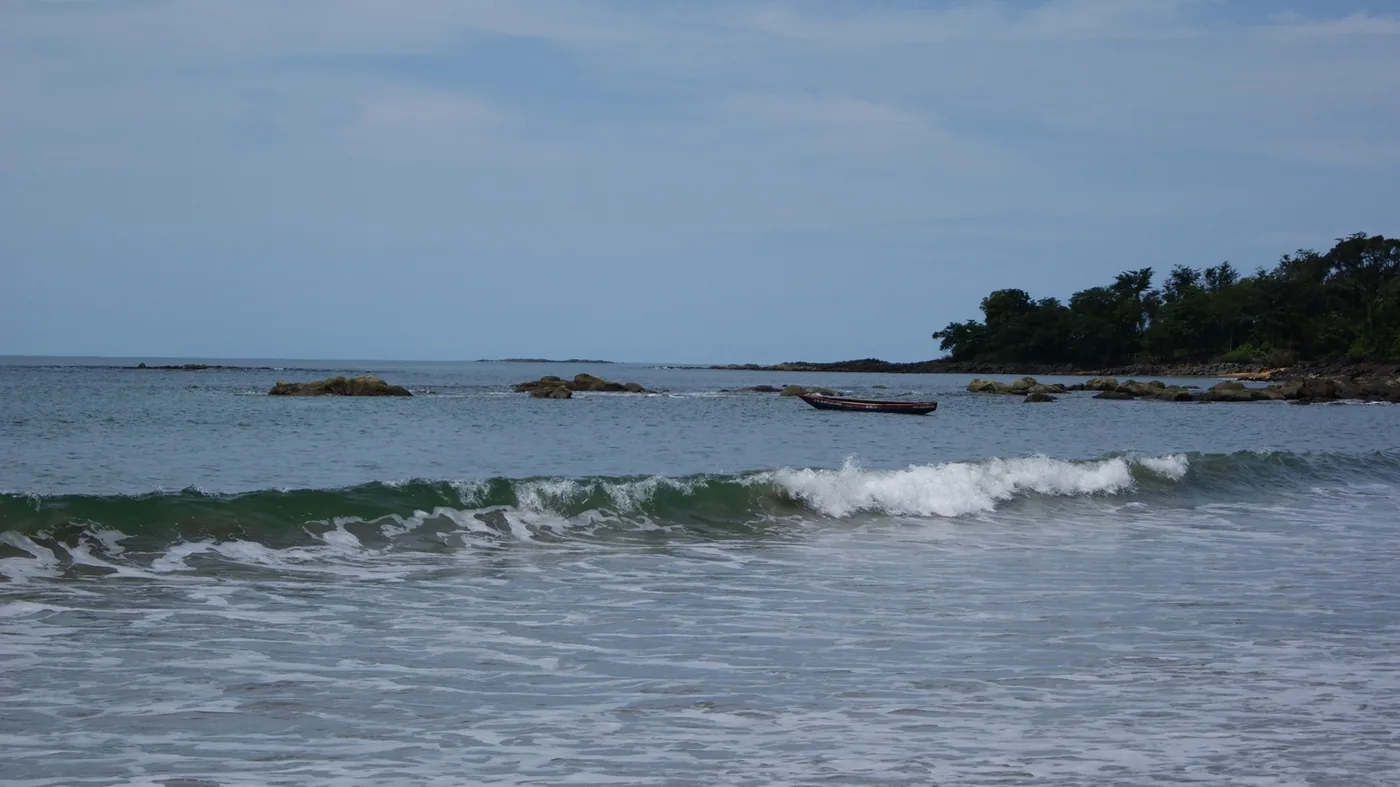 Waves breaking on a beach on the Freetown peninsula, with a wooden boat offshore
