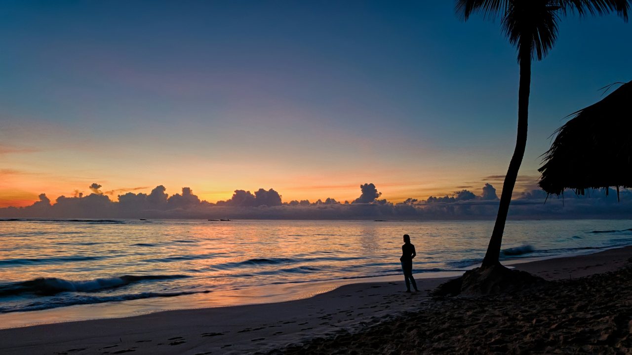 Dusk on a Dominican beach, with a single palm and a thatched shelter