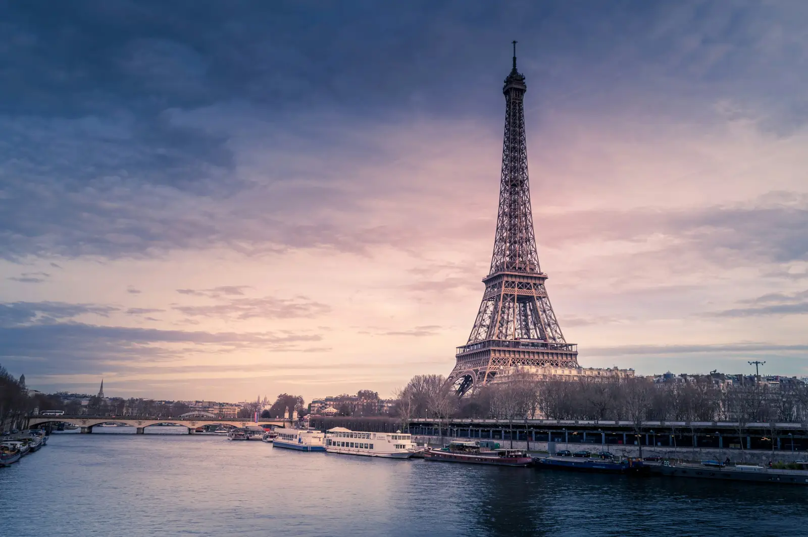 The Eiffel Tower above the Seine at dusk, barges moored along the quay